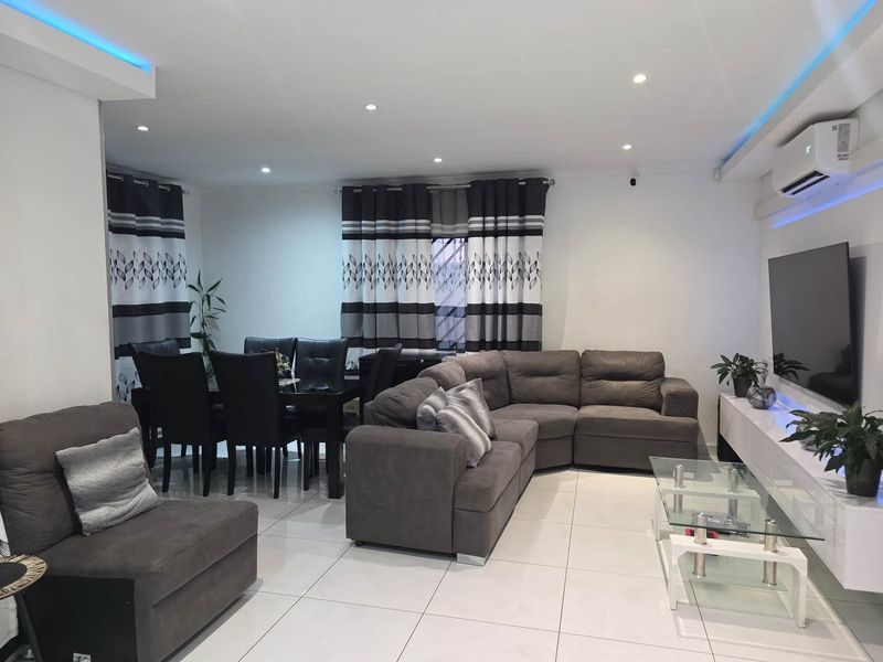 Modern open-plan living and dining area featuring tiled floors, recessed ceiling lighting, ambient LED strips, and a wall-mounted split-system air conditioner.