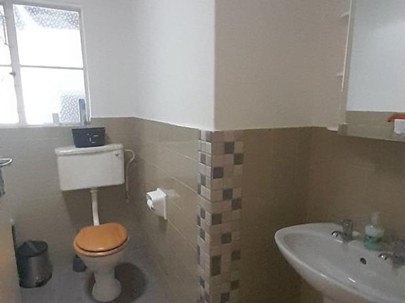 A functional bathroom featuring a pedestal washbasin, toilet, and neutral tiled splashback finishes.