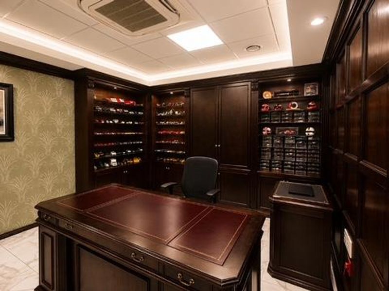 A sophisticated home office featuring custom dark wood cabinetry, elegant wall paneling, marble flooring, and integrated recessed lighting with a coffered ceiling design.
