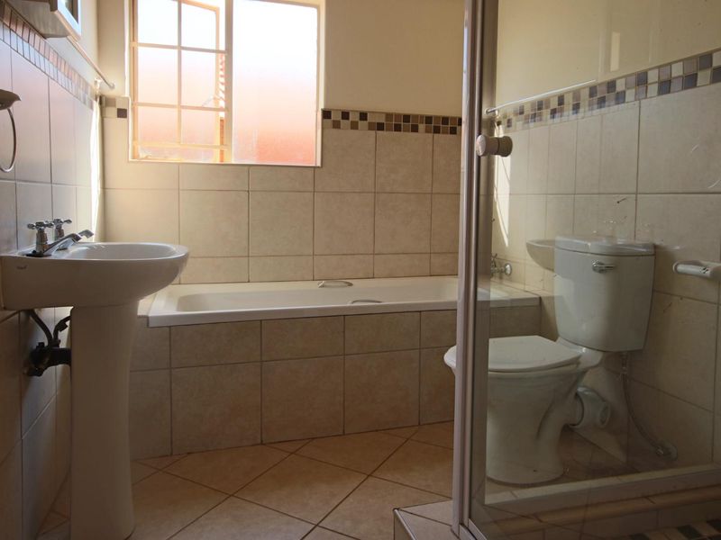 A functional bathroom featuring a pedestal basin, built-in bathtub, toilet, and a separate shower enclosure with neutral wall and floor tiling.