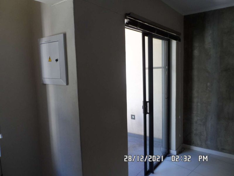 An empty living area featuring tiled flooring, a built-in electrical distribution board, and a sliding glass door leading to an outdoor space.