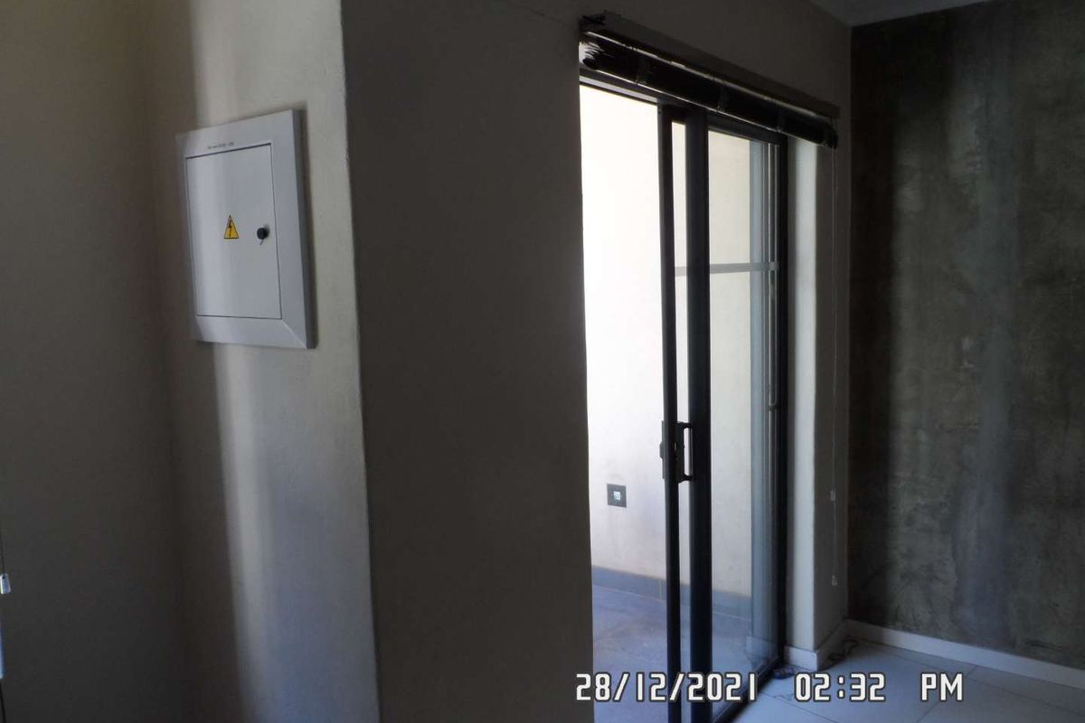 An empty living area featuring tiled flooring, a built-in electrical distribution board, and a sliding glass door leading to an outdoor space.