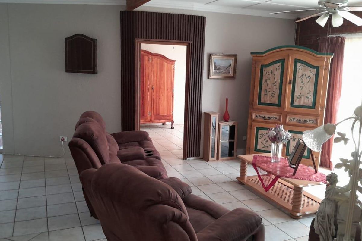A living room featuring tiled flooring, a ceiling fan, and a unique glass block wall section, leading into an adjacent room.