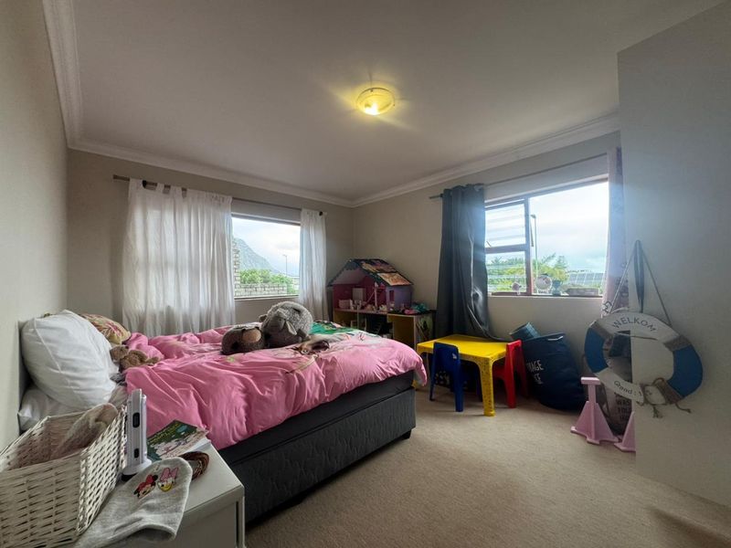 A well-lit bedroom featuring neutral wall tones, carpeted flooring, and dual windows with aluminium frames, offering a comfortable and functional living space.