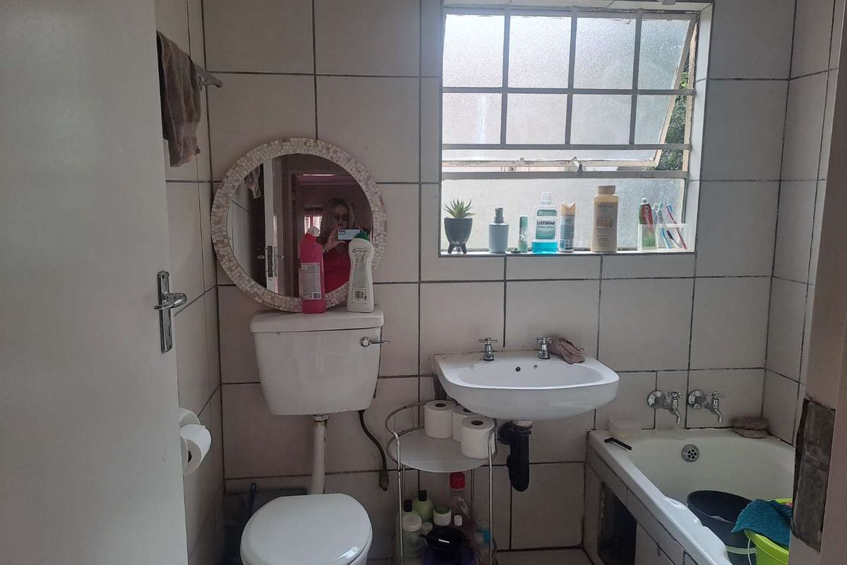 Compact bathroom featuring a standard toilet, pedestal basin, and bathtub with tiled walls and a window for natural light.