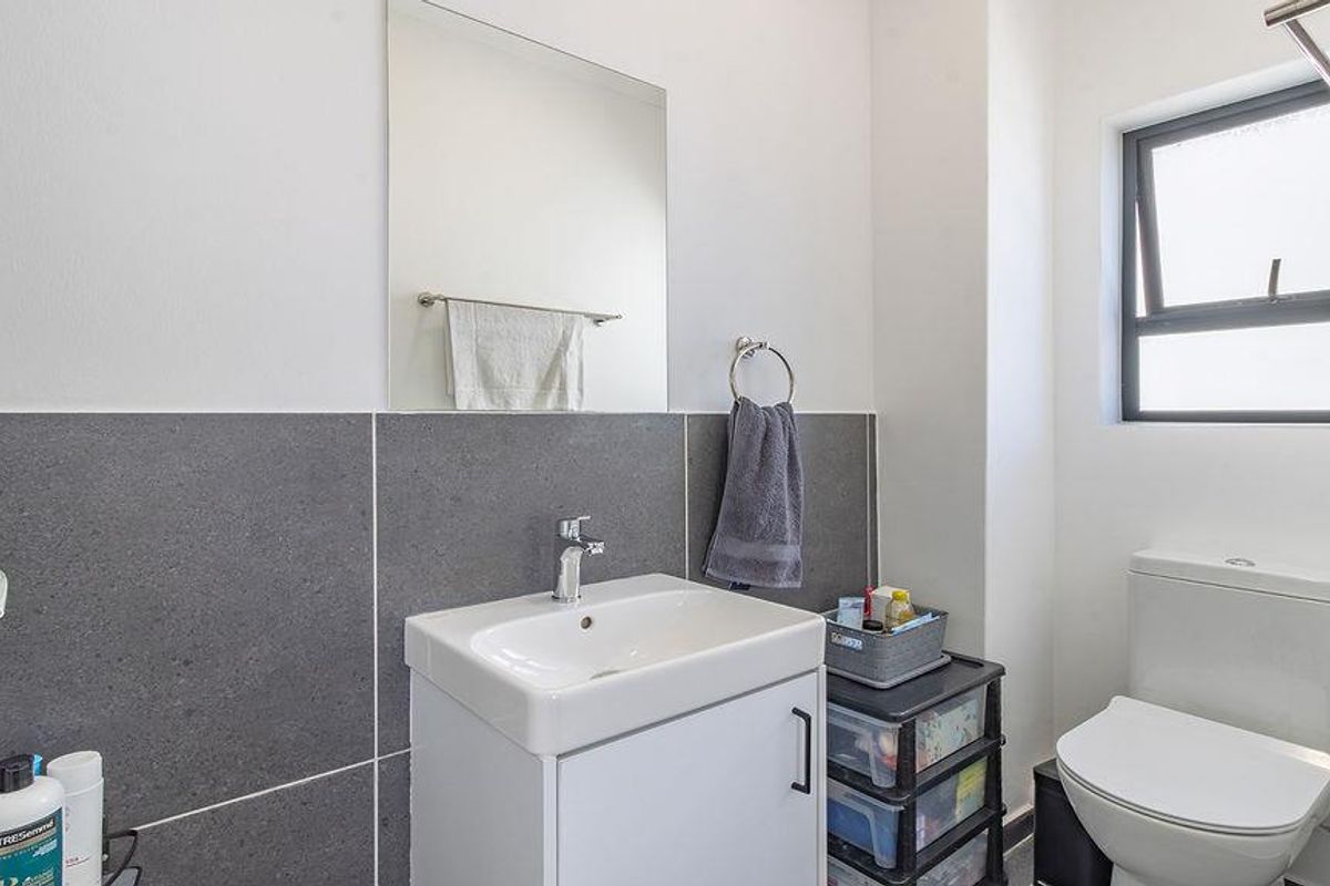 A modern bathroom featuring a vanity with a basin, a wall-mounted mirror, a toilet, and dark grey tiled wall accents.