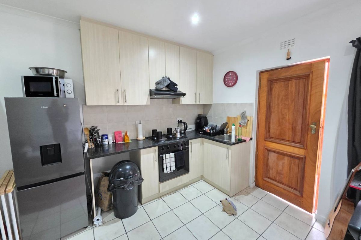 Functional kitchen featuring light-toned cabinetry, dark laminate countertops, built-in oven with extractor fan, and tiled flooring, providing a practical workspace.
