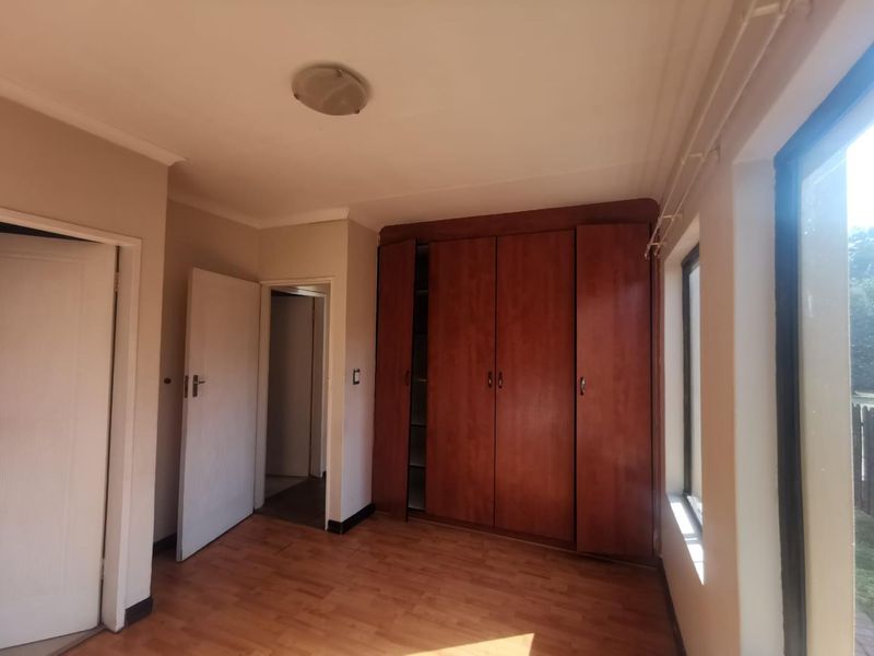 A vacant bedroom featuring built-in wooden cupboards, laminate flooring, and large windows allowing for natural light.