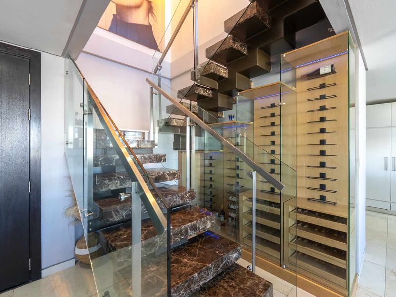 Elegant entrance hallway featuring a striking marble staircase with glass balustrades and a sophisticated integrated glass-enclosed wine cellar.