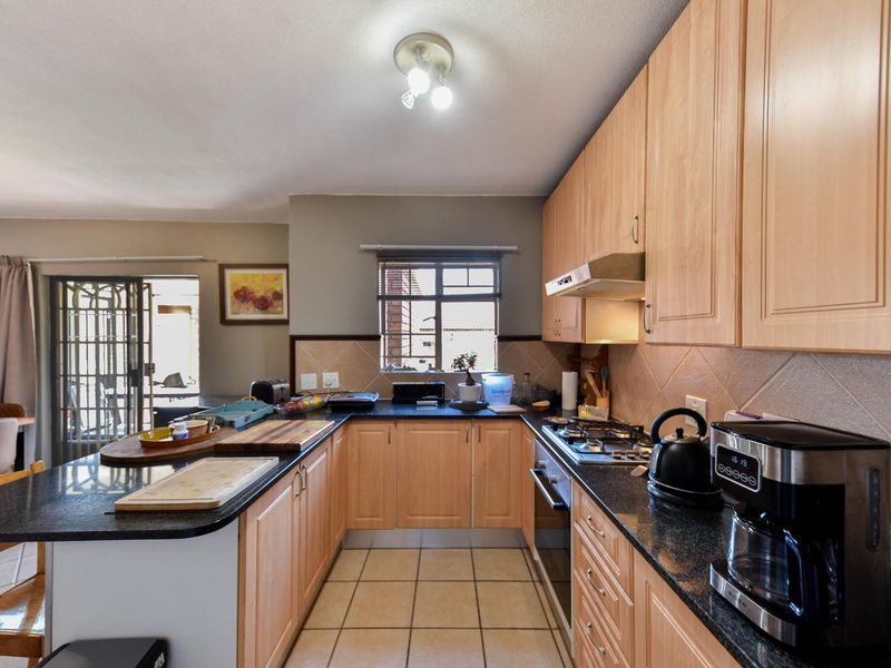 Functional kitchen featuring light wood cabinetry, granite countertops, gas hob, and tiled flooring, with direct access to an outdoor patio area.
