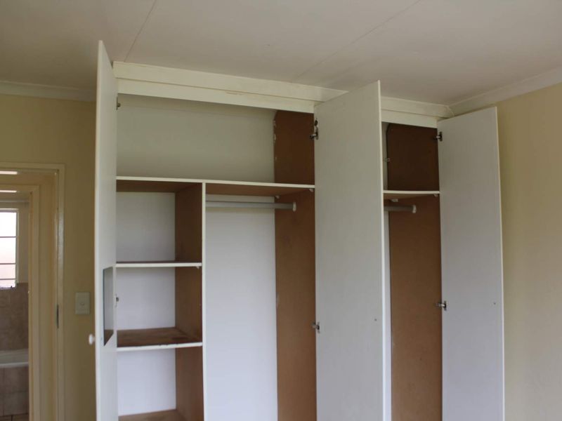 A bedroom featuring a built-in wardrobe with internal shelving and hanging rails, showing signs of wear and dated finishes.