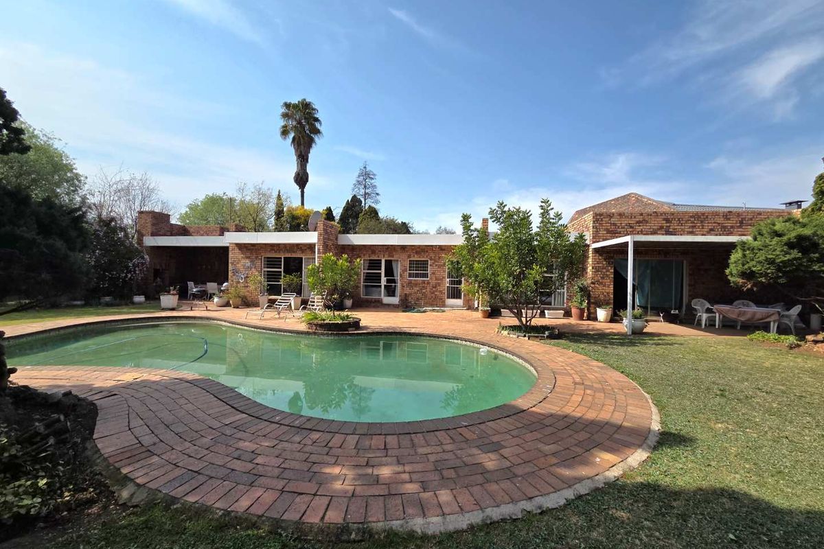 Rear exterior view featuring a swimming pool, brick-paved surround, and a covered patio area attached to the main brick residence.
