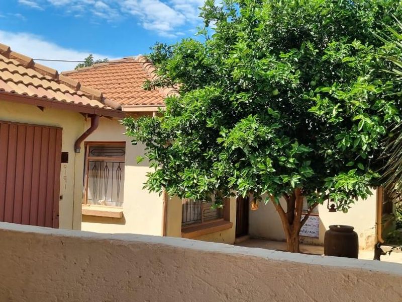 A view of the rear exterior of the house featuring terracotta roof tiles, security-barred windows, and a masonry boundary wall.