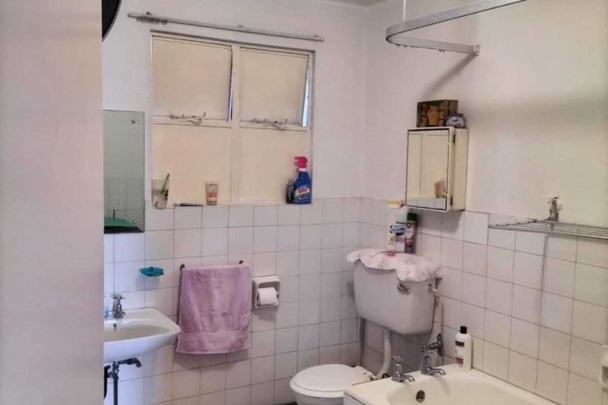 A functional bathroom featuring a bathtub, wall-mounted basin, and toilet, with tiled walls and a dated finish, offering potential for modernization and renovation.