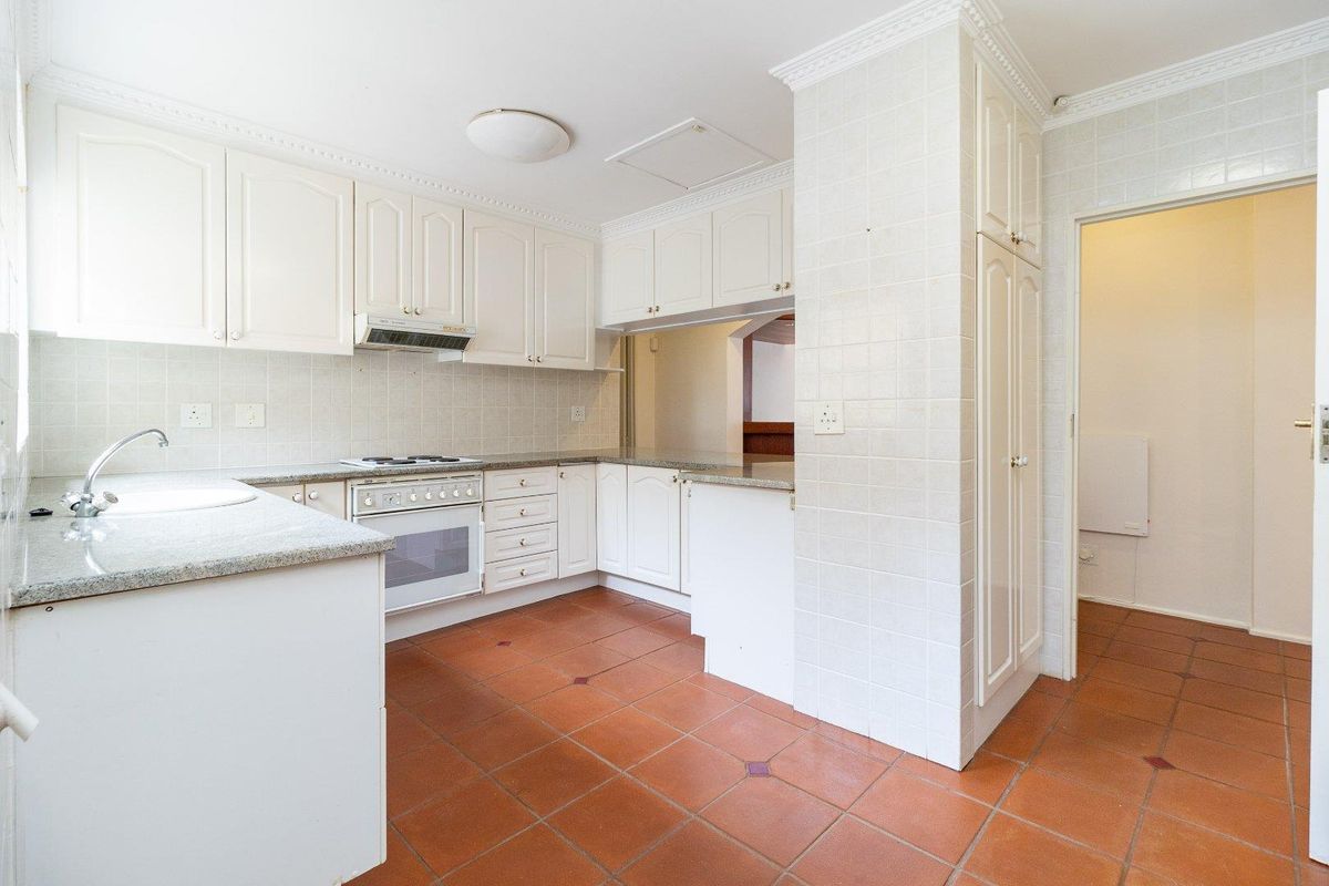 A functional kitchen featuring white cabinetry, granite countertops, a built-in oven and hob, and tiled flooring with a pass-through window to the adjacent room.