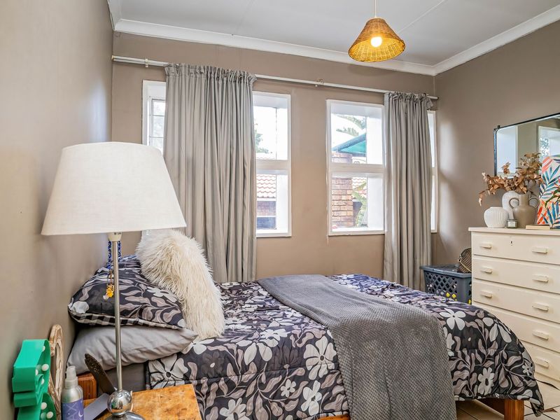 A cozy bedroom featuring tiled flooring, neutral wall tones, and dual windows with curtain tracks, providing a functional and comfortable living space.