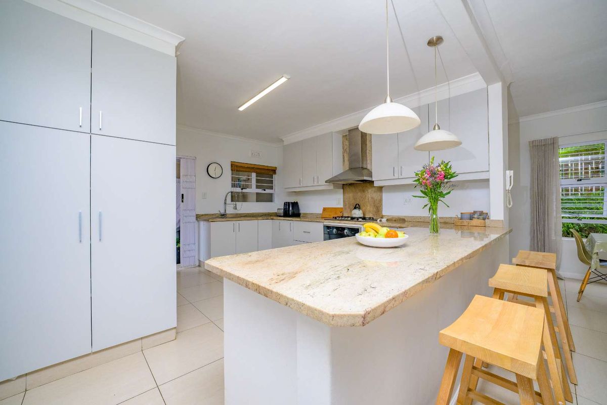 Modern kitchen featuring granite countertops, ample built-in cabinetry, a gas hob with extractor fan, and a breakfast bar island with pendant lighting.
