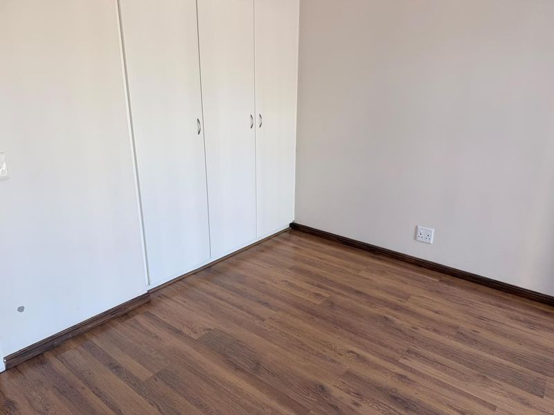 A clean, empty bedroom featuring modern laminate flooring and white built-in cupboards, providing a neutral canvas for personalization.