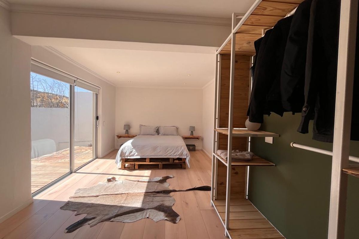 Spacious bedroom featuring light wood flooring, built-in open shelving, and large sliding glass doors providing direct access to an outdoor deck area.