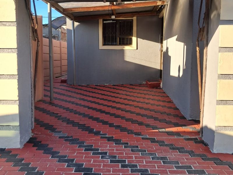 A paved driveway area featuring a metal carport structure and a secure window, providing functional off-street parking space.