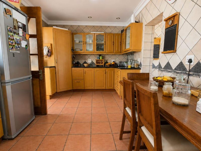 A functional kitchen featuring wooden cabinetry, tiled backsplash, and terracotta-style floor tiles, offering a traditional layout with integrated storage and dining space.