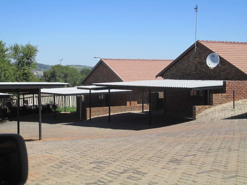 Exterior view of a residential apartment complex featuring covered carport parking bays and brick building facades with tiled roofing.