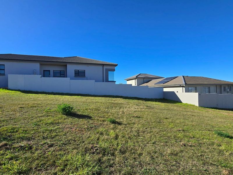A view of a vacant residential plot featuring a gentle slope, bordered by established boundary walls and adjacent modern residential properties.