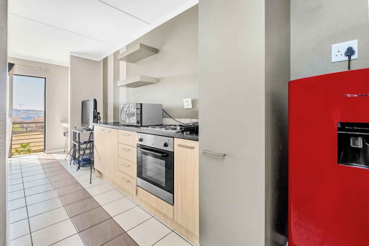 A compact kitchen featuring light wood cabinetry, a built-in oven, and a hob, with direct access to a balcony area.