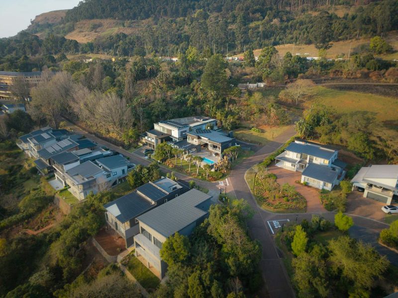 An aerial view of a modern residential estate featuring multiple homes, landscaped surroundings, paved access roads, and private swimming pools.
