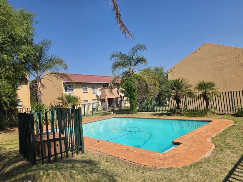 Communal swimming pool area featuring brick coping, metal fencing, and landscaped surroundings within an apartment complex setting.