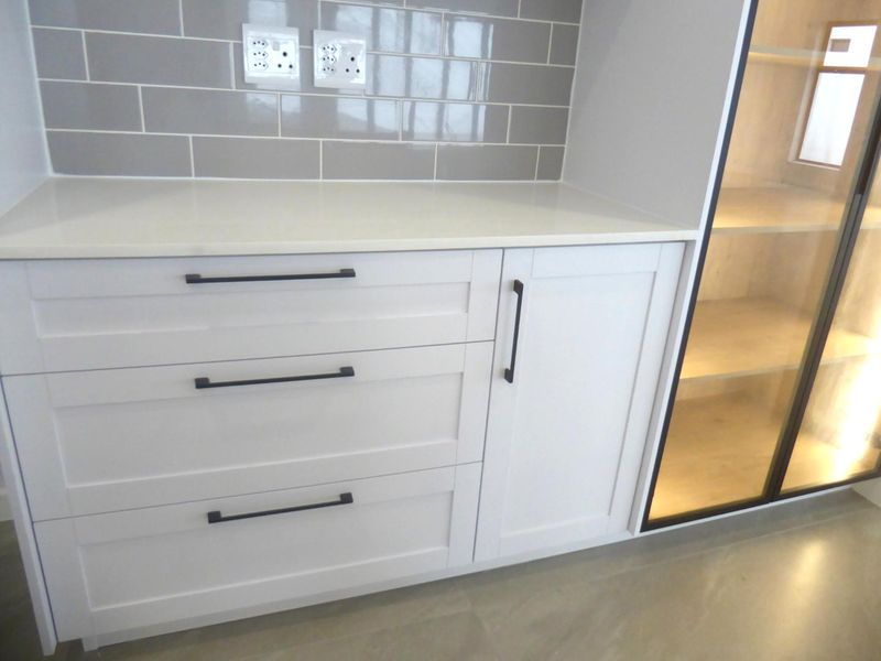 Modern kitchen cabinetry featuring white shaker-style drawers, quartz countertops, grey subway tile backsplash, and an integrated glass-front display cabinet with internal lighting.