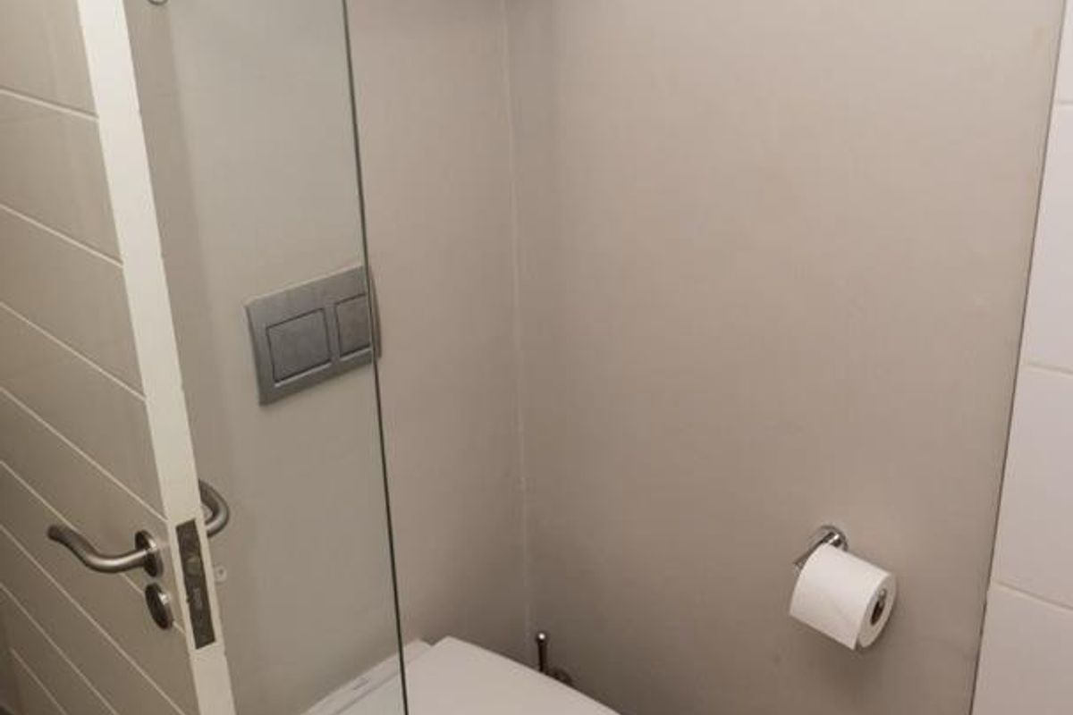 A modern bathroom featuring a wall-mounted toilet with a concealed cistern, glass shower screen, and wood-look floor tiles.