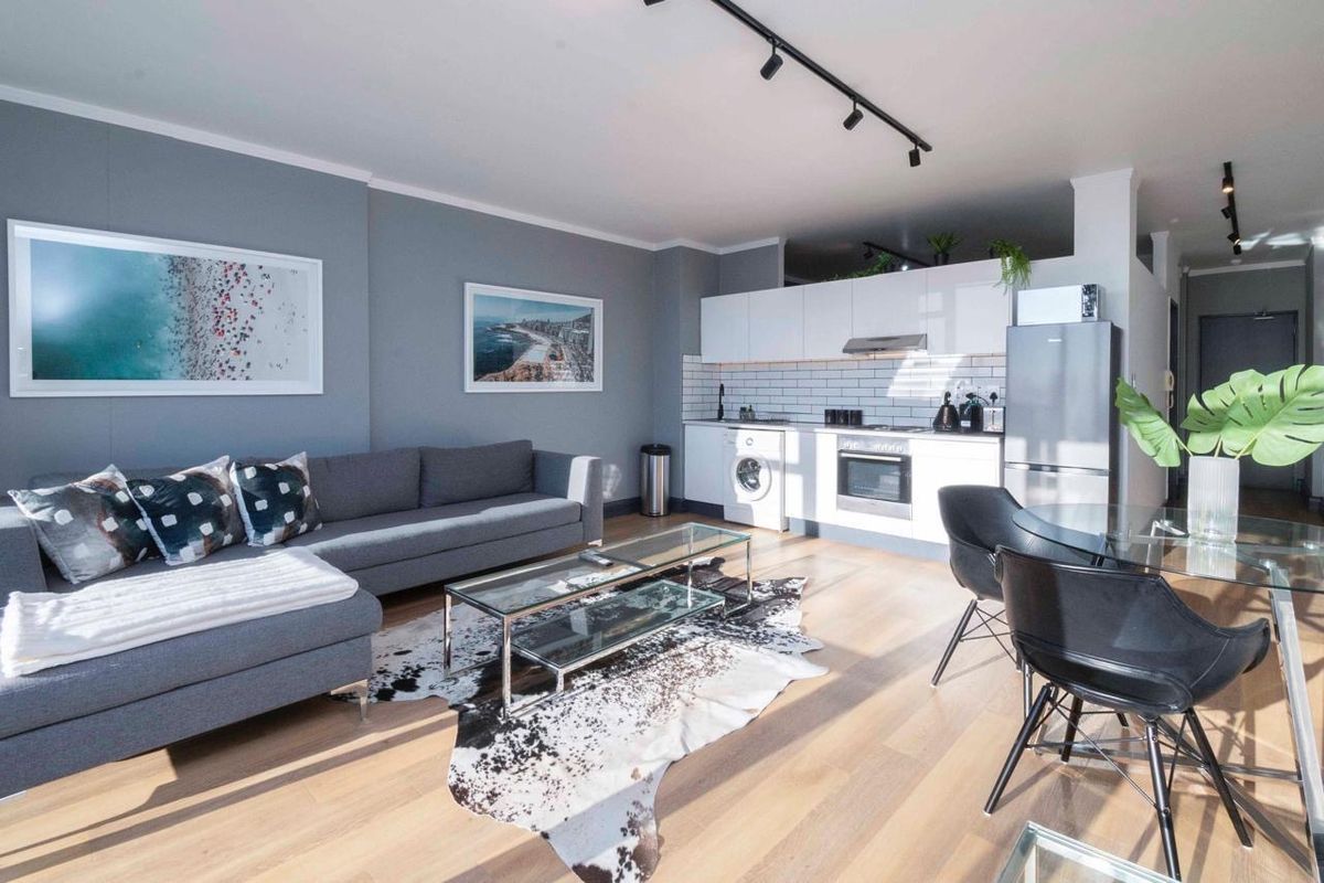 Modern open-plan living area featuring laminate flooring, track lighting, and a contemporary kitchen with subway tile backsplash and integrated appliances.