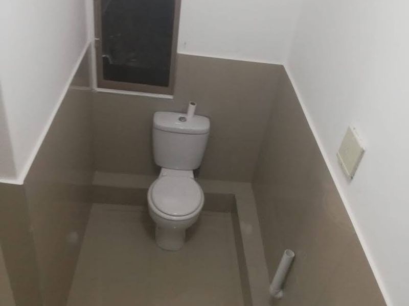 A compact bathroom featuring a toilet and pedestal basin with neutral wall tiling and a window for natural light.