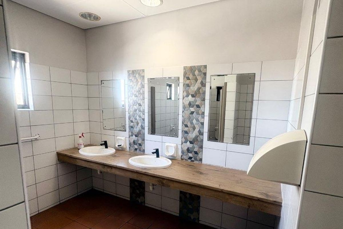 A clean office restroom featuring a dual-basin vanity with a wooden countertop, tiled walls, and modern recessed lighting.