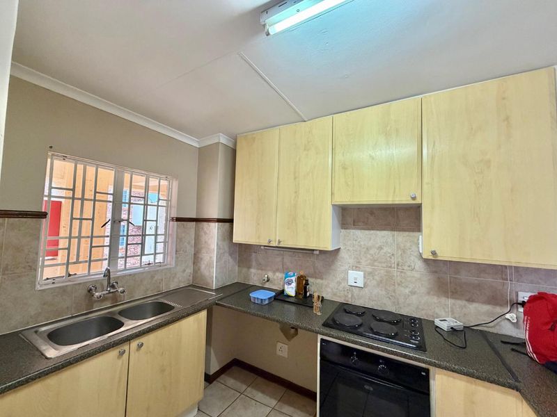 Functional kitchen featuring light wood cabinetry, tiled backsplash, double basin sink, and built-in electric oven and hob with security bars on the window.