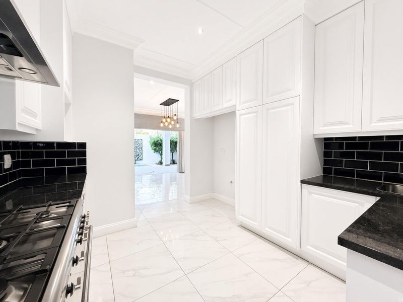 Modern kitchen featuring white cabinetry, black subway tile backsplash, granite countertops, gas cooktop, and polished porcelain floor tiles with a view to the patio.