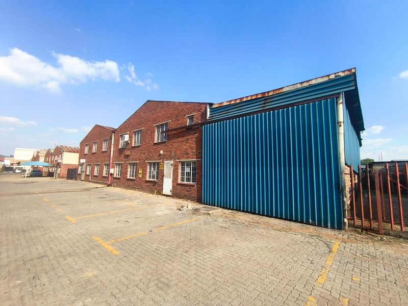 Industrial property exterior featuring a combination of brick and corrugated metal cladding with an adjacent paved parking area.