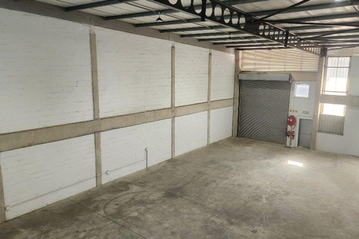 Spacious industrial warehouse unit featuring high ceilings with exposed steel trusses, concrete flooring, and a large roller shutter door for easy access.