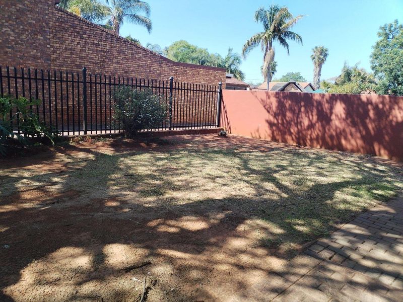 A private rear garden area featuring a brick boundary wall, metal security fencing, and a paved walkway.