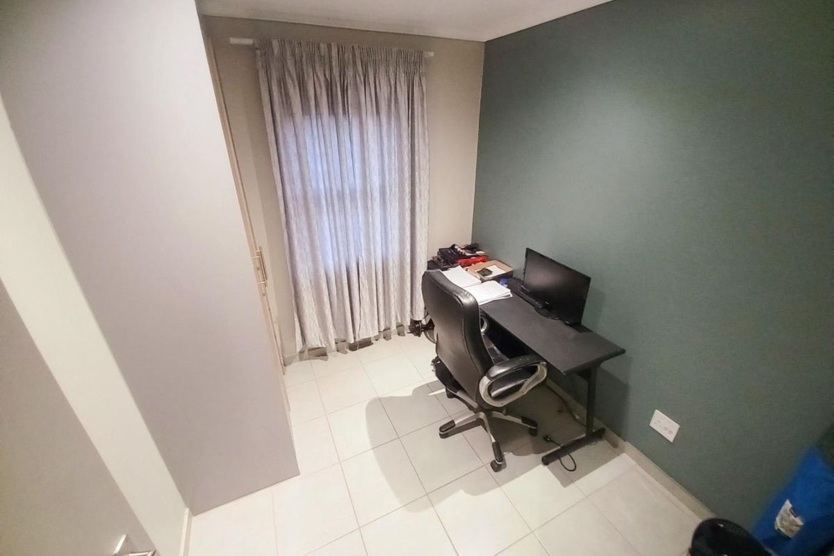 A compact bedroom or home office featuring tiled flooring, a built-in wardrobe, and a feature wall.