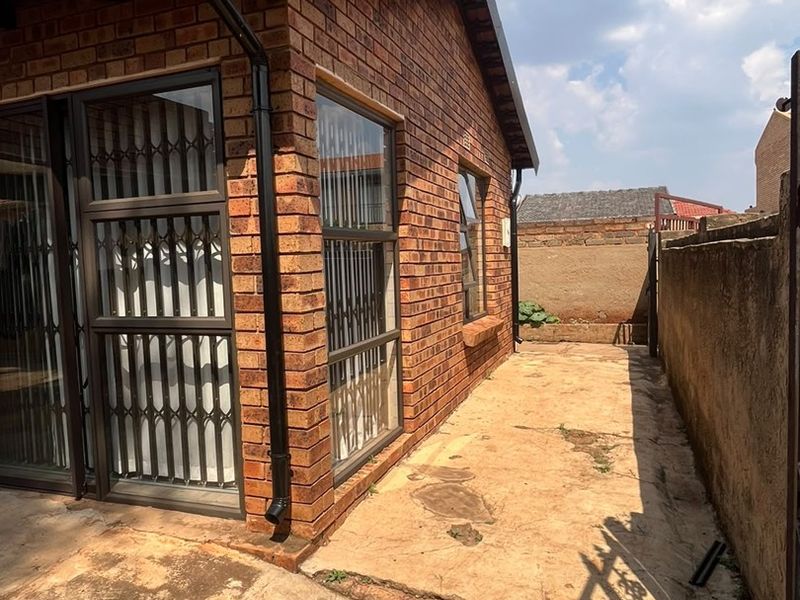 Rear exterior view of the house featuring face brick walls, aluminium window frames with security gates, and a paved side walkway.