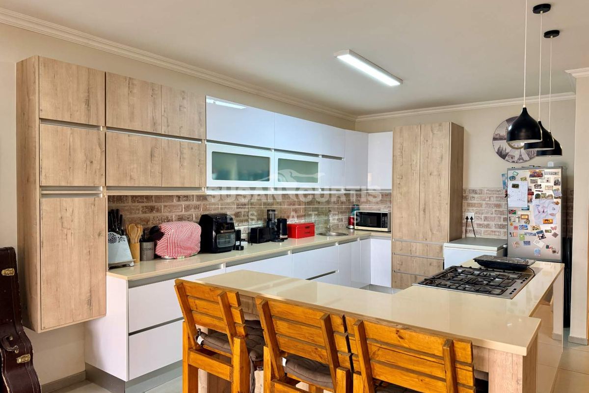Modern kitchen featuring light wood and white cabinetry, stone countertops, a gas hob, and a decorative brick-style backsplash.