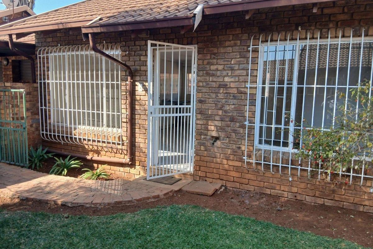 Rear exterior view of a face brick townhouse featuring a tiled roof, security bars on windows, and a security gate entrance.