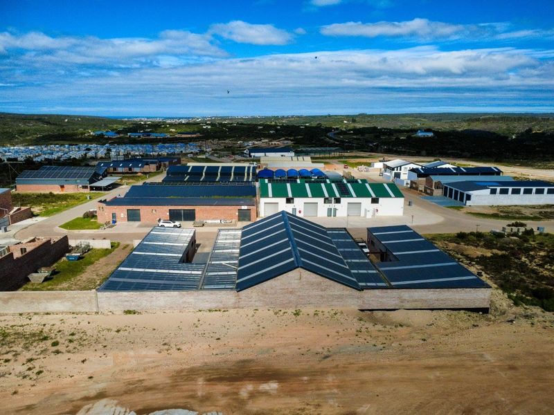 Aerial view of a commercial industrial complex featuring multiple warehouse buildings with extensive solar panel installations and paved access roads.