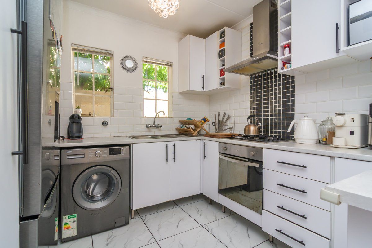 Compact kitchen featuring white cabinetry, subway tile backsplash, mosaic feature wall, built-in oven, gas hob, and marble-look floor tiles.