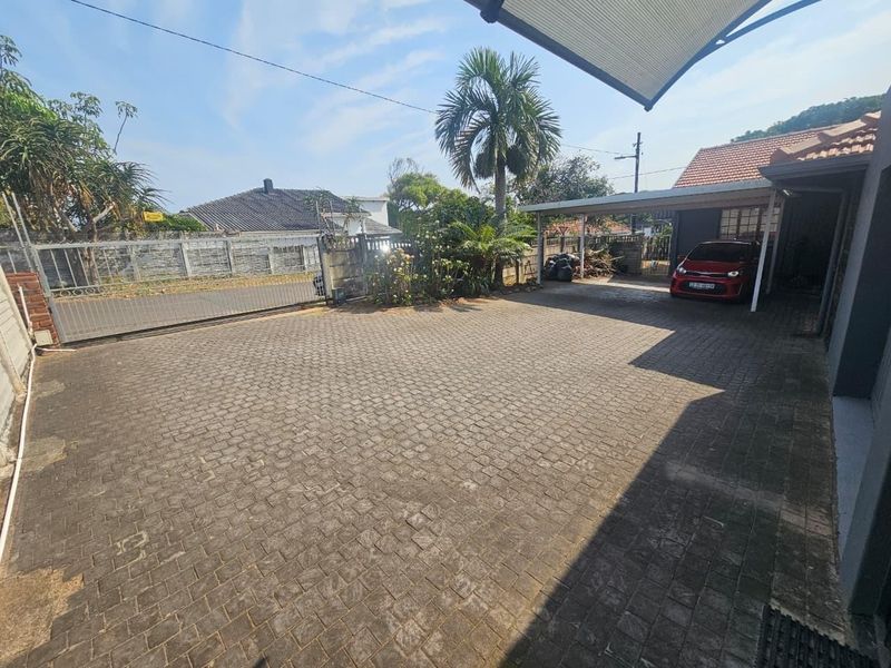 Spacious paved driveway and carport area providing secure off-street parking with perimeter boundary walls and a sliding gate.