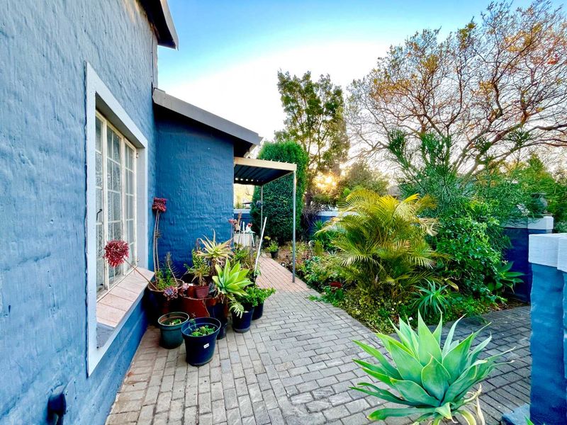 A side view of the townhouse featuring a paved walkway, a small covered patio area, and established garden landscaping.