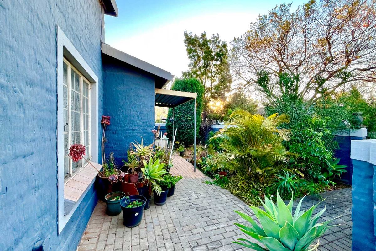 A side view of the townhouse featuring a paved walkway, a small covered patio area, and established garden landscaping.