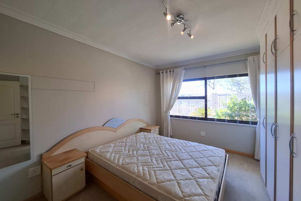 A well-lit bedroom featuring built-in wardrobes, neutral wall finishes, and a large window providing natural light and garden views.